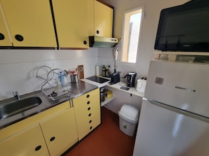 A compact kitchen with yellow cabinets, a stainless steel sink, a white refrigerator, and a window providing natural light. - Charming secure T2 in Collioure with parking near the beach (Collioure)