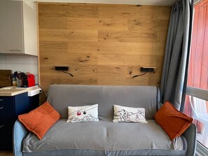 Ein gemütliches Zimmer mit einem hölzernen Kopfteil, einem grauen Sofa mit orangefarbenen Kissen und einem fenster mit Vorhängen.