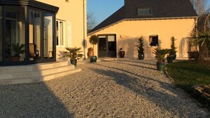 A two-story house with a gravel driveway and potted plants. - Charming Renovated Cottage with Pool and Art near Le Mans (Lucé-sous-Ballon)