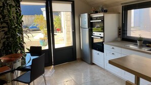 A compact kitchen with a sliding glass door leading to a patio, a built-in oven, and a sink with a potted plant on the counter. - Charming Renovated Cottage with Pool and Art near Le Mans (Lucé-sous-Ballon)