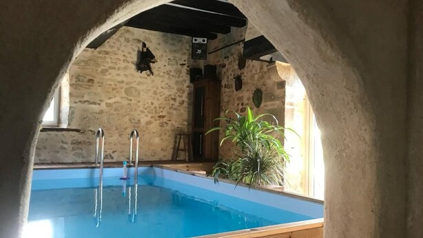An indoor swimming pool with clear water, wooden poolside, stone walls, and a potted plant. - Charming Renovated Cottage with Pool and Art near Le Mans (Lucé-sous-Ballon)