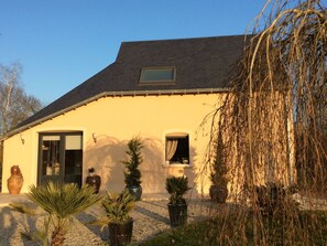A house with a sloped roof, a front door, and windows. There are potted plants in the front yard. - Charming Renovated Cottage with Pool and Art near Le Mans (Lucé-sous-Ballon)