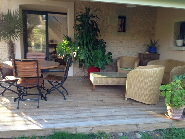 An outdoor patio with a wooden deck, wicker furniture, and potted plants. - Charming Renovated Cottage with Pool and Art near Le Mans (Lucé-sous-Ballon)