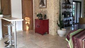 A room with a wooden door, a red cabinet, a white table with a bar stool, a large potted plant, and a bookshelf with various items. - Charming Renovated Cottage with Pool and Art near Le Mans (Lucé-sous-Ballon)