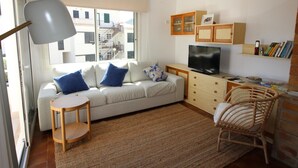 Un salon moderne avec un canapé, un téléviseur, une petite table et des fauteuils en osier.