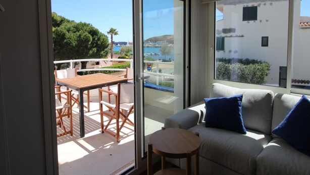 Un balcon avec une table et des chaises, un canapé avec des coussins et une vue sur la mer et les bâtiments.