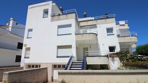 Un immeuble à plusieurs étages doté de balcons, d’un escalier et d’une entrée fermée par un portail.