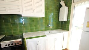 Une cuisine avec des carreaux verts, des armoires blanches, une cuisinière et un évier.