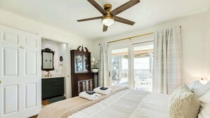 A bedroom with a large bed, a ceiling fan, a dresser, a mirror, and a view of the outdoors. - Pink Pearl - Where Mr Ocean Blue Meets Ms Posh Pink! (Surfside Beach)