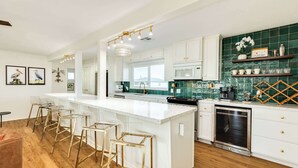 A modern kitchen with white cabinetry, a central island with stools, a microwave, and a dishwasher. - Pink Pearl - Where Mr Ocean Blue Meets Ms Posh Pink! (Surfside Beach)