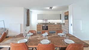 A modern dining area with a wooden table set for six, surrounded by orange chairs. - New apartment 108m², center Huez, parking, wifi, 6 guests (Huez)