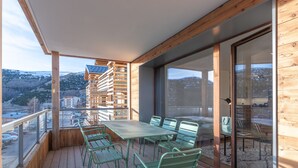 A wooden deck with a table and chairs, large windows, and a view of a mountainous area. - New apartment 108m², center Huez, parking, wifi, 6 guests (Huez)