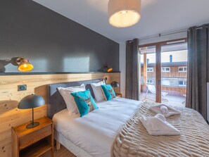 Une chambre d’hôtel avec un grand lit, une tête de lit en bois, une table de chevet avec une lampe et une vue sur le balcon extérieur.