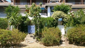 Un immeuble résidentiel doté de nombreux balcons, d’un jardin avec différentes espèces de plantes et d’un portail bleu.