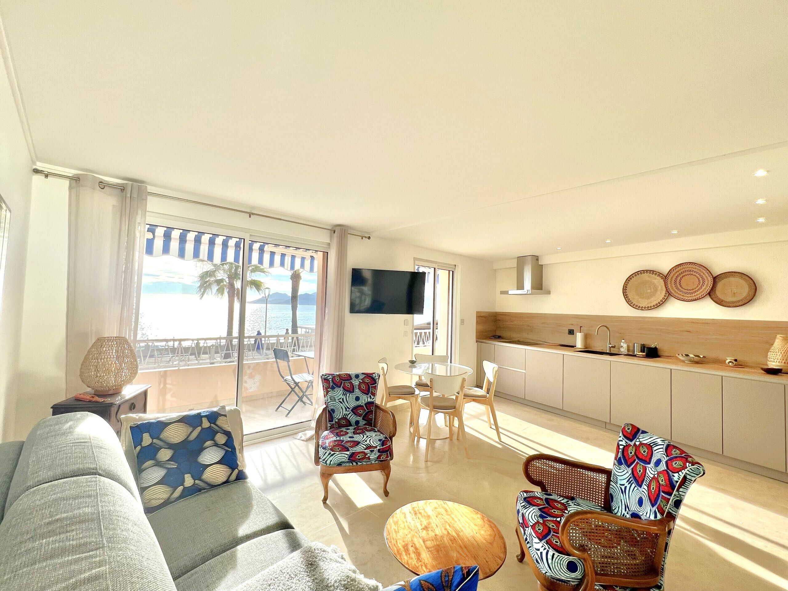 Ein modernes Wohnzimmer mit Sofa, Sesseln, einem Couchtisch und Blick auf den Strand durch große Fenster.