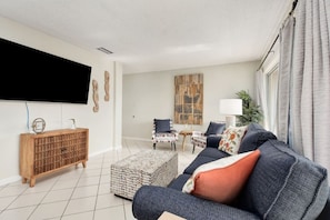 Una sala de estar moderna con sofá, reposapiés, mueble de madera y televisor de pantalla plana.