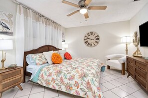 A bedroom with a bed, a ceiling fan, a clock, a nightstand, a lamp, and a dresser. - 2nd Floor King Bedroom w/Lagoon View (Destin)