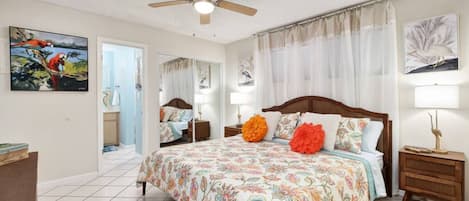 A bedroom with a large bed, a ceiling fan, and artwork on the walls.