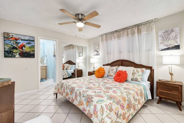 A bedroom with a large bed, a ceiling fan, and artwork on the walls.