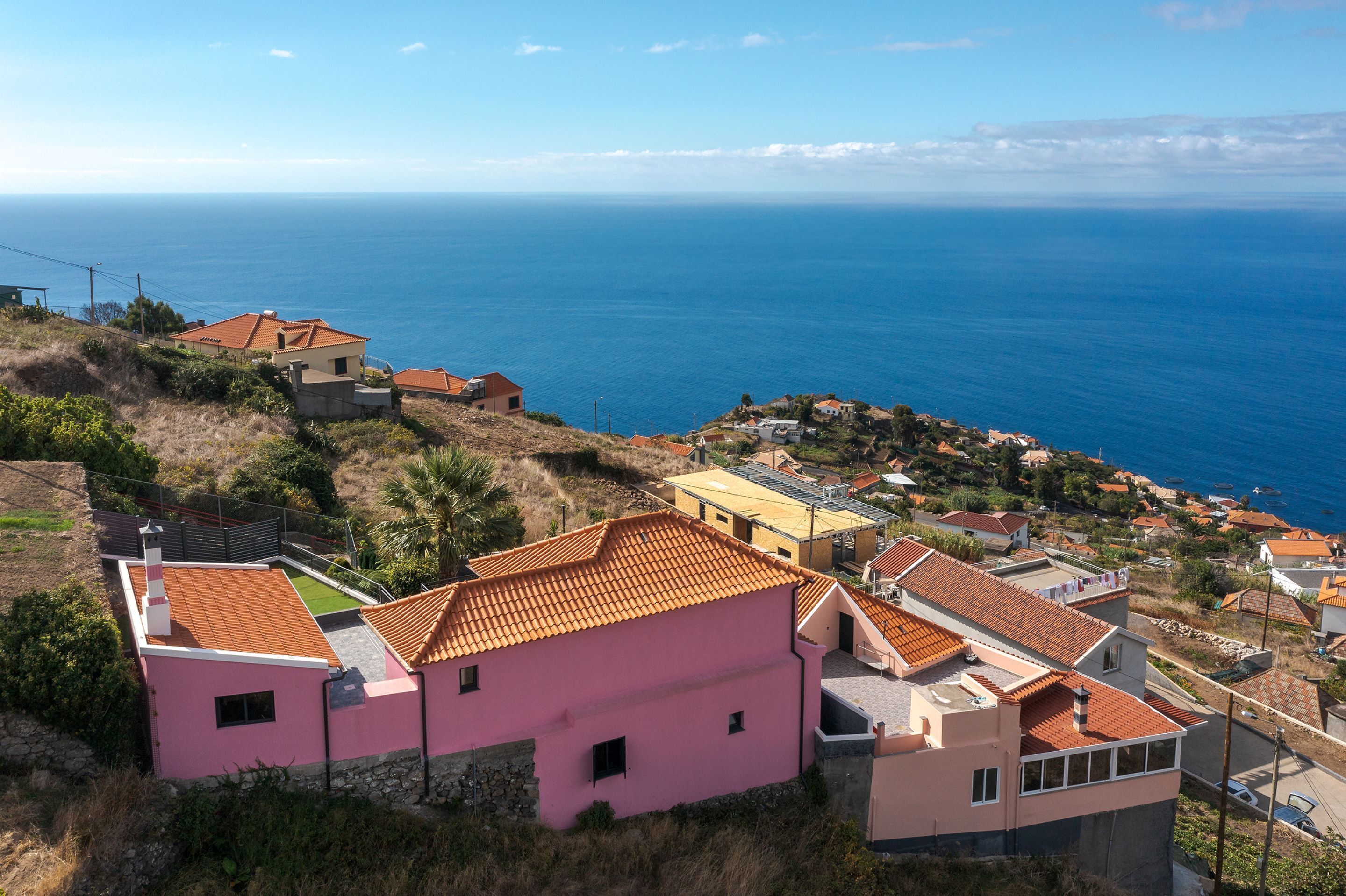 A coastal village with terracotta-roofed houses, a pink building, and a view of the sea.