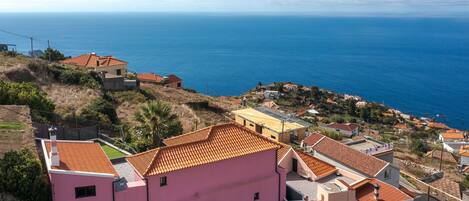 A coastal village with terracotta-roofed houses, a pink building, and a view of the sea.