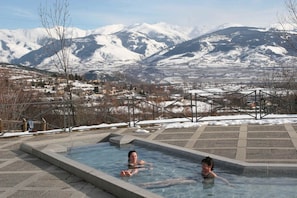 Un jacuzzi con vistas a montañas nevadas y un pueblo al fondo.