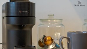 A Nespresso coffee machine, a mug, and a glass jar with coffee beans. - 2BED/2BATH Bliss | Parking - VAT Q - By Tempstay (Berkshire)