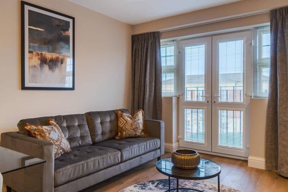 A living room with a grey sofa, a round coffee table, and a large window with blinds.