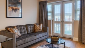 A living room with a grey sofa, a round coffee table, and a large window with blinds. - 2BED/2BATH Bliss | Parking - VAT Q - By Tempstay (Berkshire)