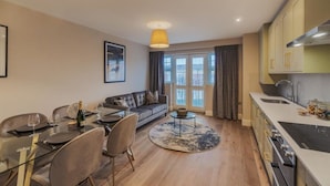 A modern apartment with a dining area, a sofa, a kitchen, and a large window. - 2BED/2BATH Bliss | Parking - VAT Q - By Tempstay (Berkshire)
