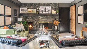 A modern living room with a stone fireplace, green sofa, and black leather ottoman. - Spacious 4BR, Games, Pool, Theater & Private Yard! (Omaha)