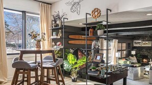 A modern living room with a round table, bar stools, a foosball table, and a fireplace. - Spacious 4BR, Games, Pool, Theater & Private Yard! (Omaha)