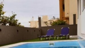A swimming pool with lounge chairs, a book, and a glass of wine on the edge. - Ezith Luxury Apartments (Heraklion)