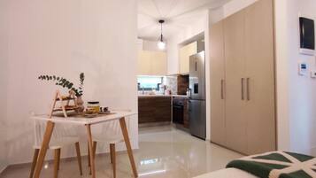 A modern kitchen with stainless steel appliances, a dining area with a white table and chairs, and a large wardrobe.