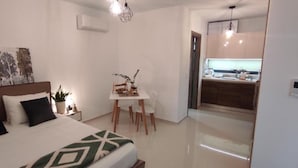 A modern hotel room with a bed, a small desk, a chair, and a kitchenette in the background. - Ezith Luxury Apartments (Heraklion)