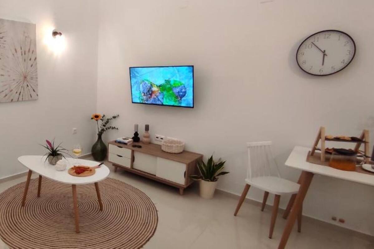 Een moderne woonkamer met een bank, salontafel, televisie en een eethoek met een stoel en een klein tafeltje.