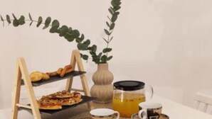 A dining table with a tray of food, a cup of coffee, and a vase with a plant. - Ezith Luxury Apartments (Heraklion)