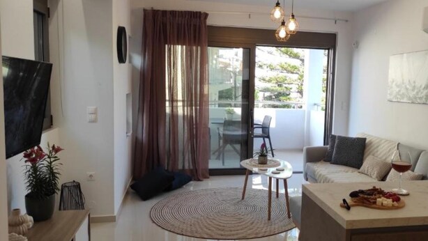 A modern living room with a sofa, a coffee table with snacks, a TV, and a large window with curtains. - Ezith Luxury Apartments (Heraklion)