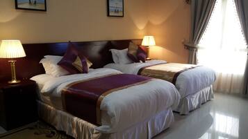 A hotel room with two beds, each with a headboard, bedside lamps, and a view of the beach through the window.
