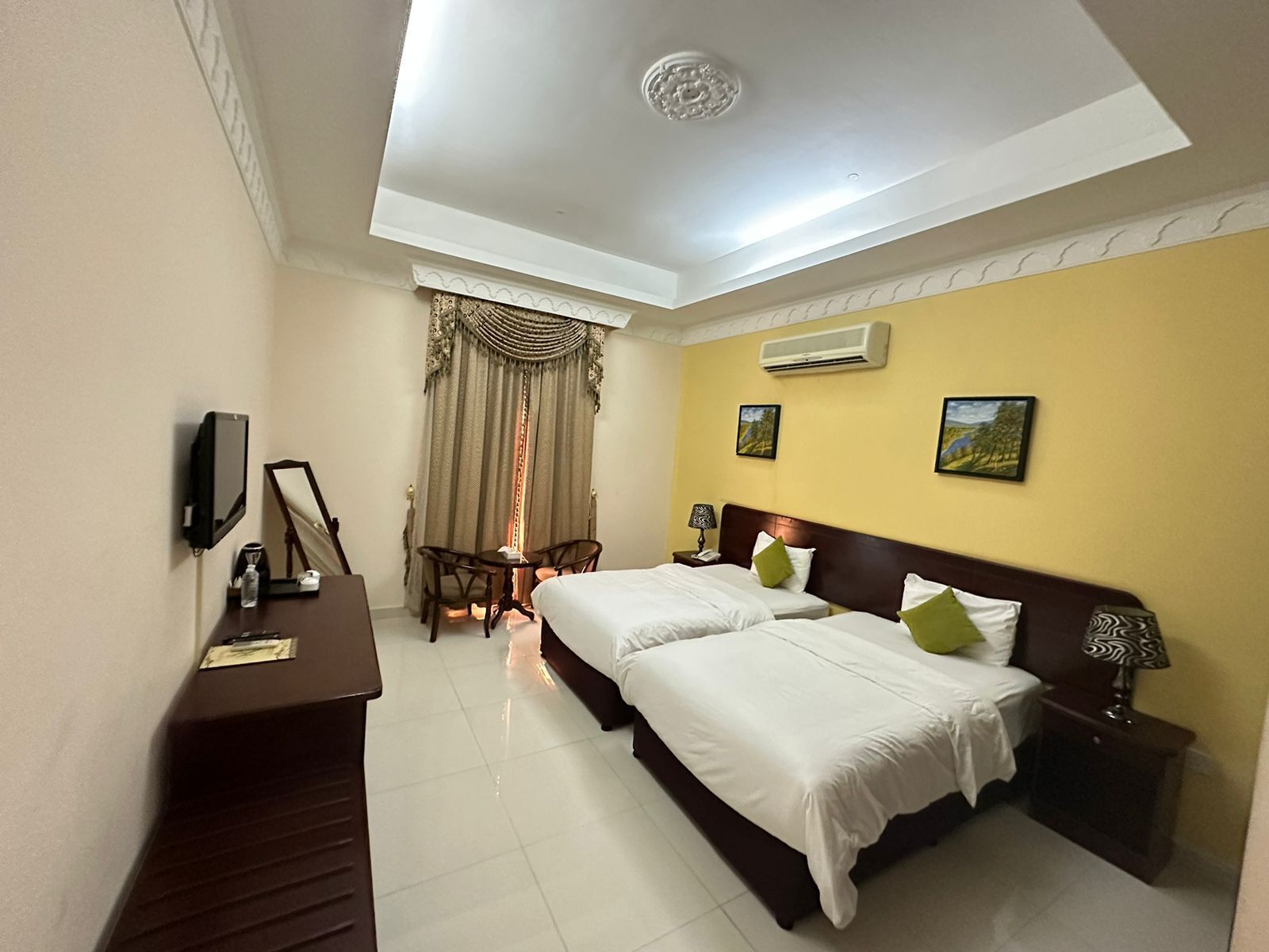A hotel room with two beds, a desk, a chair, a TV, and a window with curtains.