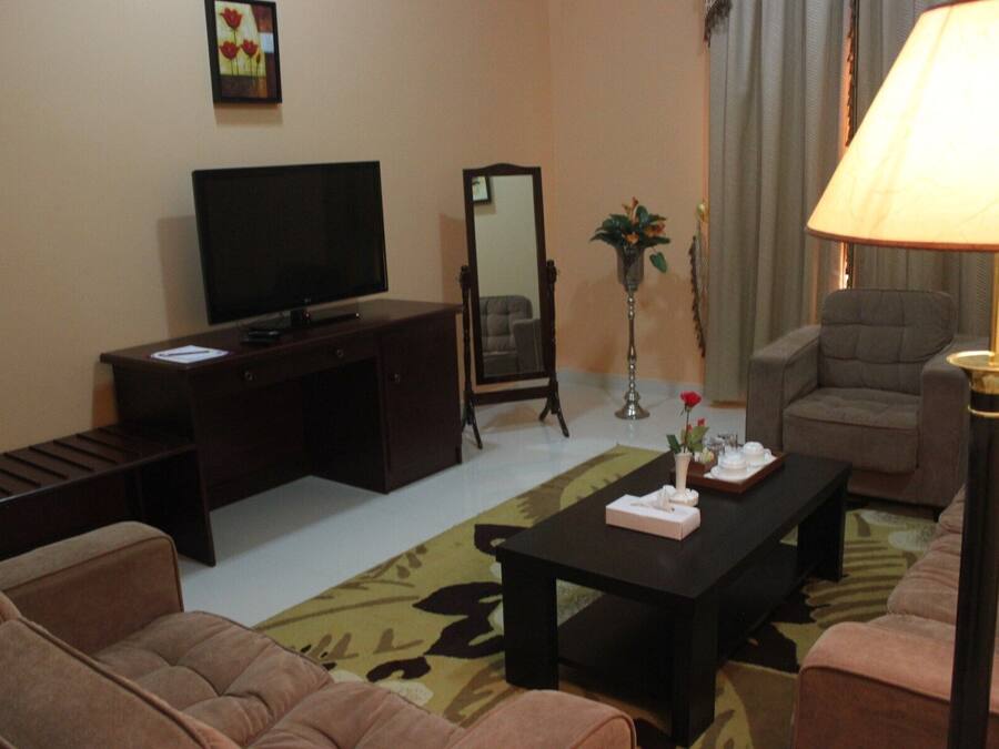 Una sala de estar con televisión, sofá, mesa de centro y lámpara.