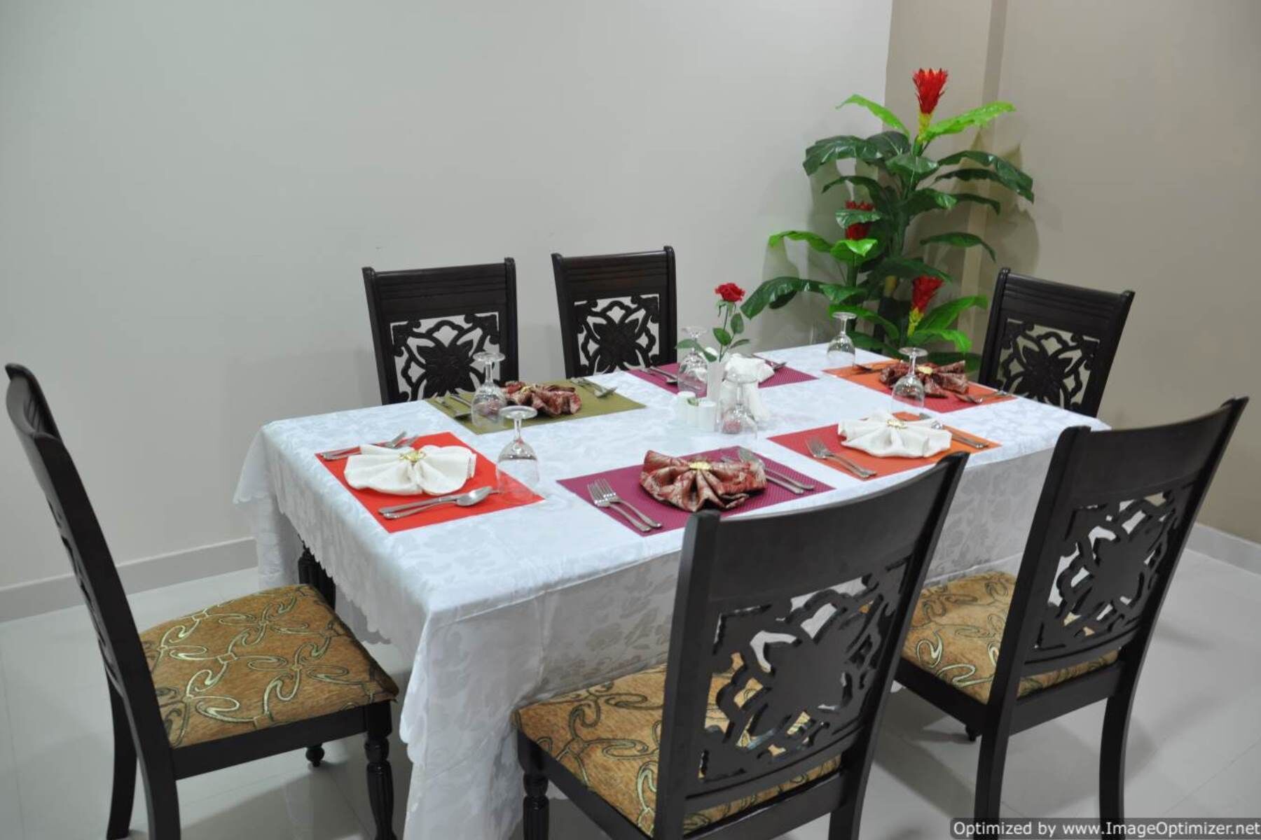 Una mesa de comedor vestida con mantel blanco, individuales rojos y un centro de mesa.