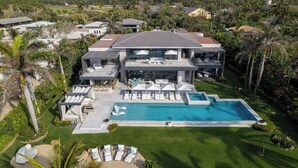 A large, modern house with a swimming pool, multiple outdoor seating areas, and a well-maintained lawn.