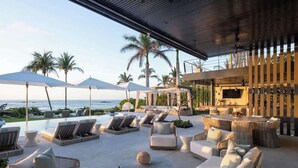 A modern outdoor lounge area with seating and umbrellas, overlooking a pool and the ocean.