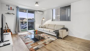 A modern living room with a sofa, coffee table, and a view through a large window. - Vintage Vibes East Freo 2B 1BA (East Fremantle)