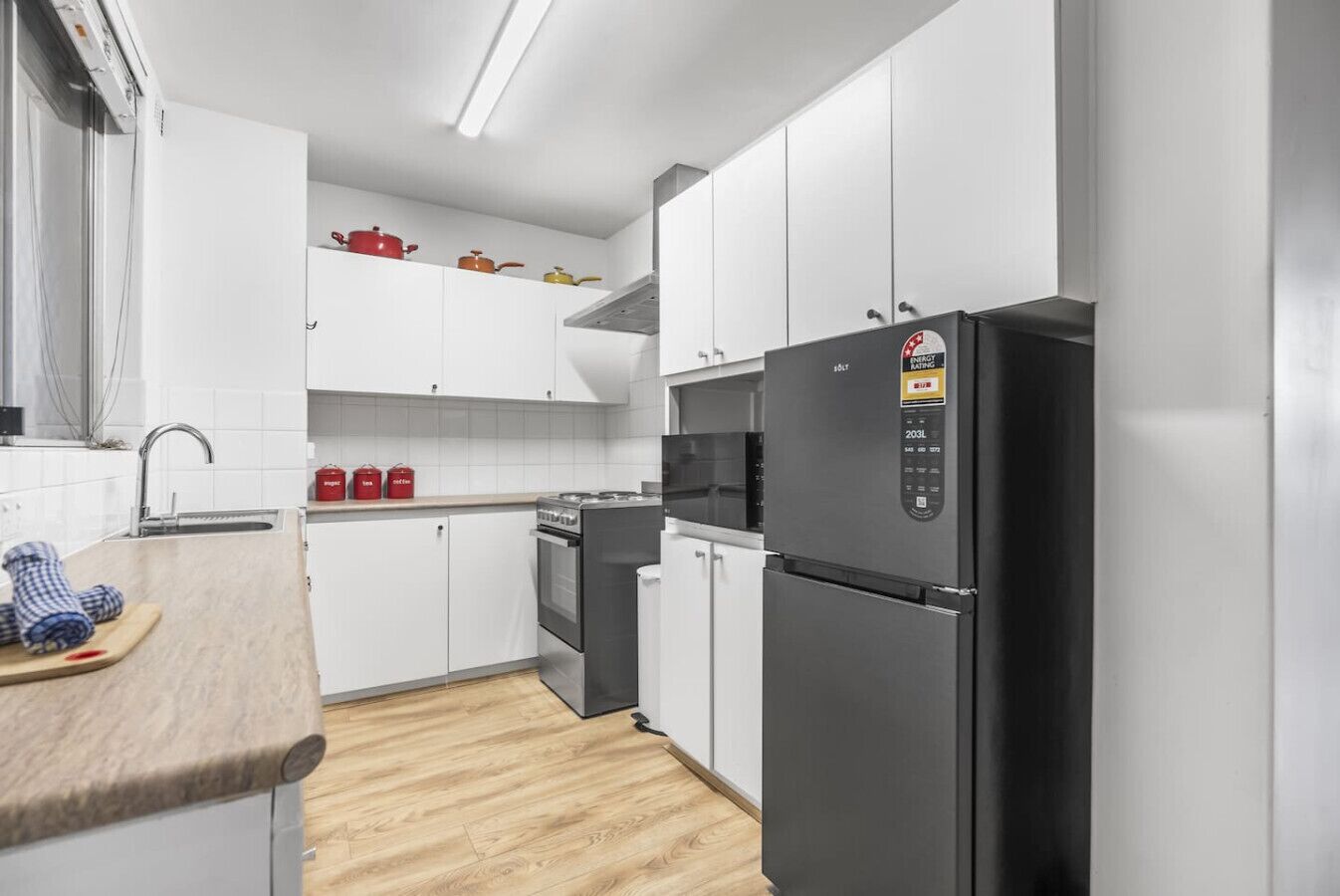 Une cuisine moderne avec des armoires blanches, un réfrigérateur noir et un plan de travail en bois.