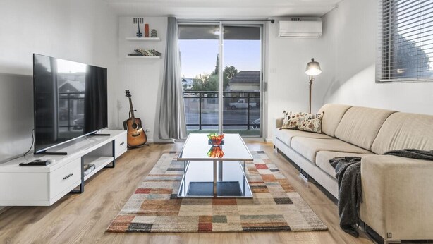 A modern living room with a flat-screen TV, a guitar, a coffee table, and a sofa. - Vintage Vibes East Freo 2B 1BA (East Fremantle)