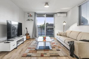 Un soggiorno moderno con una TV a schermo piatto, una chitarra, un tavolino da caffè e un divano.