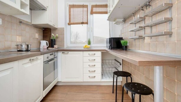 Una cocina moderna con armarios blancos, encimera de madera y ventana con persianas.