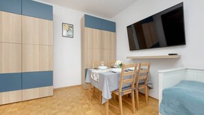 Una habitación compacta con una mesa de comedor dispuesta para dos personas, un televisor montado en la pared y una cama con cubrecama azul.